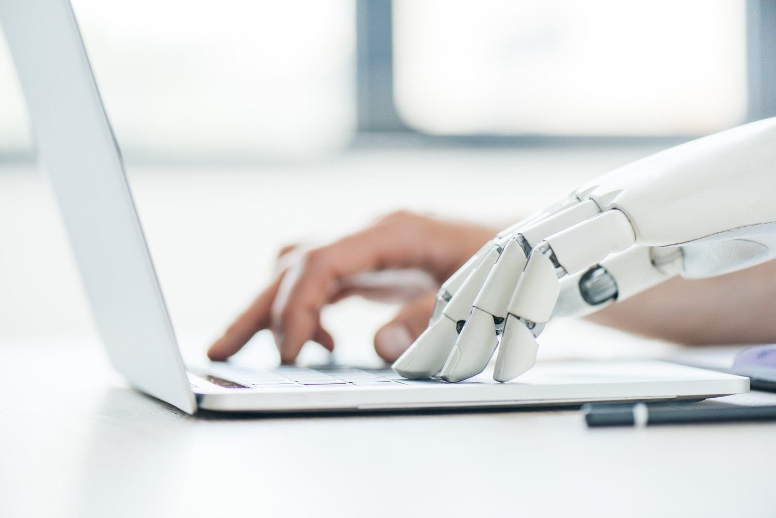 Una mano robótica y una mano humana escriben juntas en el teclado de una laptop